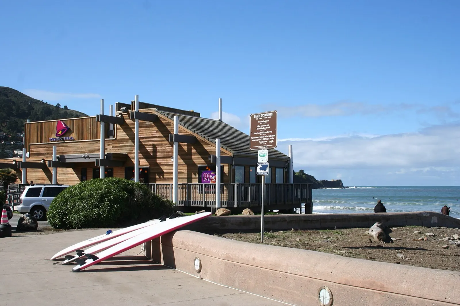 The Pacifica Taco Bell, a wood-sided building on the sand at Linda Mar Beach, with surfboards in the foreground and the ocean behind it